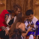 a man in a red jacket is talking to a woman while another man looks at his phone .