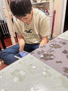 a man wearing a hollister shirt sits on a table