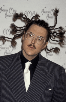 a man in a suit and tie stands in front of an american music awards wall