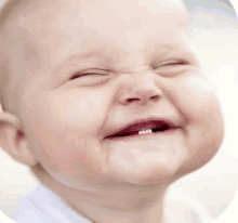 a baby is smiling with his eyes closed and his mouth open .