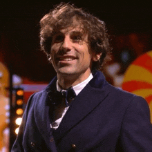 a man with curly hair wearing a blue jacket and bow tie is smiling .