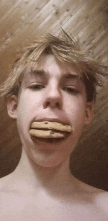 a shirtless young man with a stack of cookies in his mouth