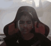 a young boy is sitting in a black and red gaming chair with his eyes closed .