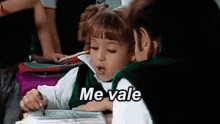 a little girl is sitting at a desk in a classroom with a book and a pen in her hand .