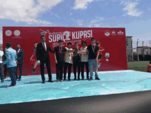 a group of people standing in front of a large red sign that says suricil kupasi