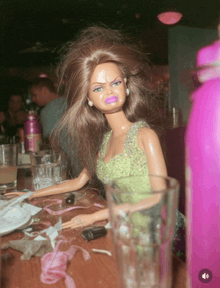 a barbie doll is sitting on a messy table with a pink bottle in the foreground