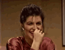 a woman in a red shirt is smiling while covering her mouth with her hand .