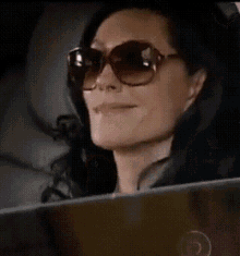 a woman wearing sunglasses is smiling and looking out the window