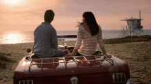 a man and a woman are sitting in the back of a car on the beach looking at the ocean .