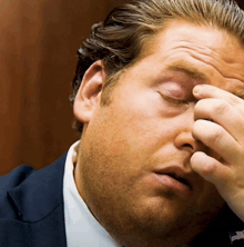 a man in a suit and tie is covering his eyes with his hand