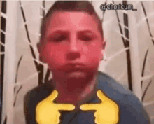 a young boy with a red face is making a funny face and pointing at the camera .