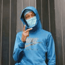 a man wearing a blue hoodie and a mask on his face is pointing at the camera .