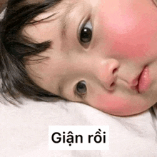 a baby with red cheeks is laying on a bed with a foreign language sticker on his face .