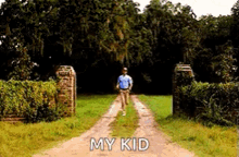 a man is walking down a dirt road with the words `` my kid '' written on the ground .