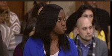 a woman in a blue jacket is sitting in a courtroom with a group of people .