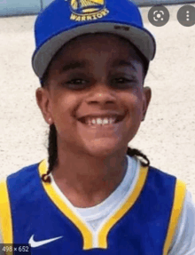 a young boy is wearing a golden state warriors hat and smiling .