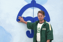 a man wearing a green jacket with the number 299 on it stands in front of a blue umbrella