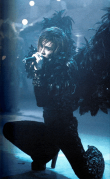 a woman in a black feathered outfit sings into a microphone