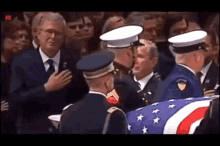 a man in a suit and tie stands in front of a group of soldiers holding an american flag .