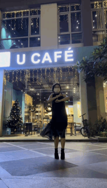 a woman in a mask stands in front of a sign that says u cafe