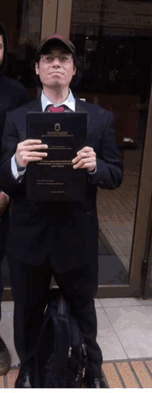 a man in a suit and tie holds up a black book with the letter m on it