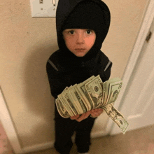 a young boy in a black hooded jacket holds a stack of 20 dollar bills