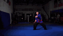 a man kneeling on a blue mat in a gym with a sign above him that says ' martial arts academy '