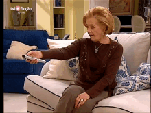 an elderly woman is sitting on a couch holding a remote control .