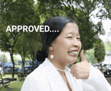 a woman giving a thumbs up in front of a sign that says " approved "