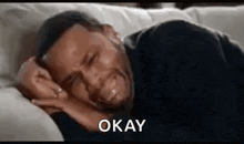 a man is crying while laying on a couch and saying okay .