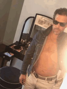 a shirtless man wearing sunglasses takes a picture of himself in front of a mirror