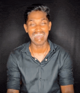 a man wearing a black shirt and a necklace smiles for the camera