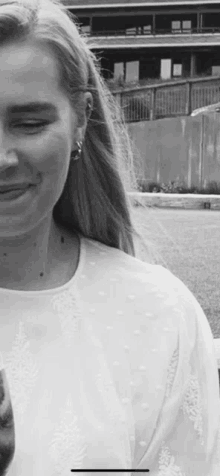 a black and white photo of a woman wearing a white shirt and earrings smiling .