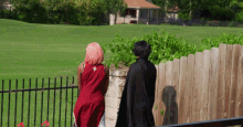 a woman in a red dress and a man in a black cape are standing next to a wooden fence