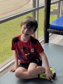 a young boy wearing a red spiderman shirt sits on the ground