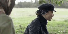 a woman wearing a hat and a bandana is sitting in a field with a netflix logo in the background