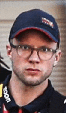 a man wearing glasses , a hat and a polo shirt is looking at the camera .