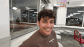 a young man wearing a brown shirt that says principle smiles in a diner