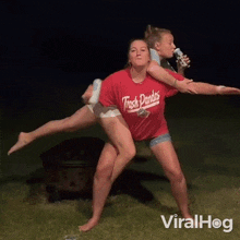 a woman in a trash pandas shirt is carrying another woman on her back while another woman drinks a beer .