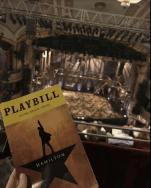 a person holding a playbill for hamilton in front of a theater