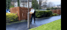 a man carrying a box of pizza is standing next to a pole