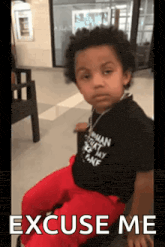 a young boy is sitting in a chair with the words excuse me written on the bottom of the picture .