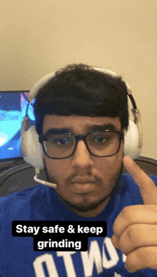 a man wearing headphones and a blue shirt that says " stay safe and keep grinding "