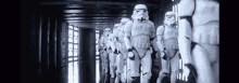 a row of stormtroopers are walking down a hallway in a black and white photo .