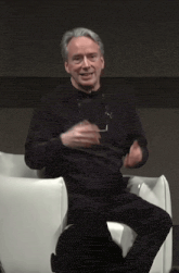 a man wearing glasses is sitting in a chair and smiling