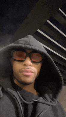 a man wearing a black hoodie and sunglasses looks at the camera