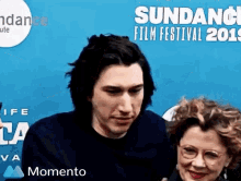 a man and a woman are standing next to each other in front of a blue wall at the sundance film festival .