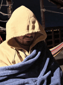 a man wearing a hooded sweatshirt is wrapped in a blue towel