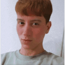 a young man with red hair is wearing a grey shirt and looking at the camera
