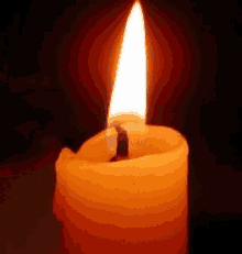 a close up of a lit candle in the dark with a flame coming out of it .